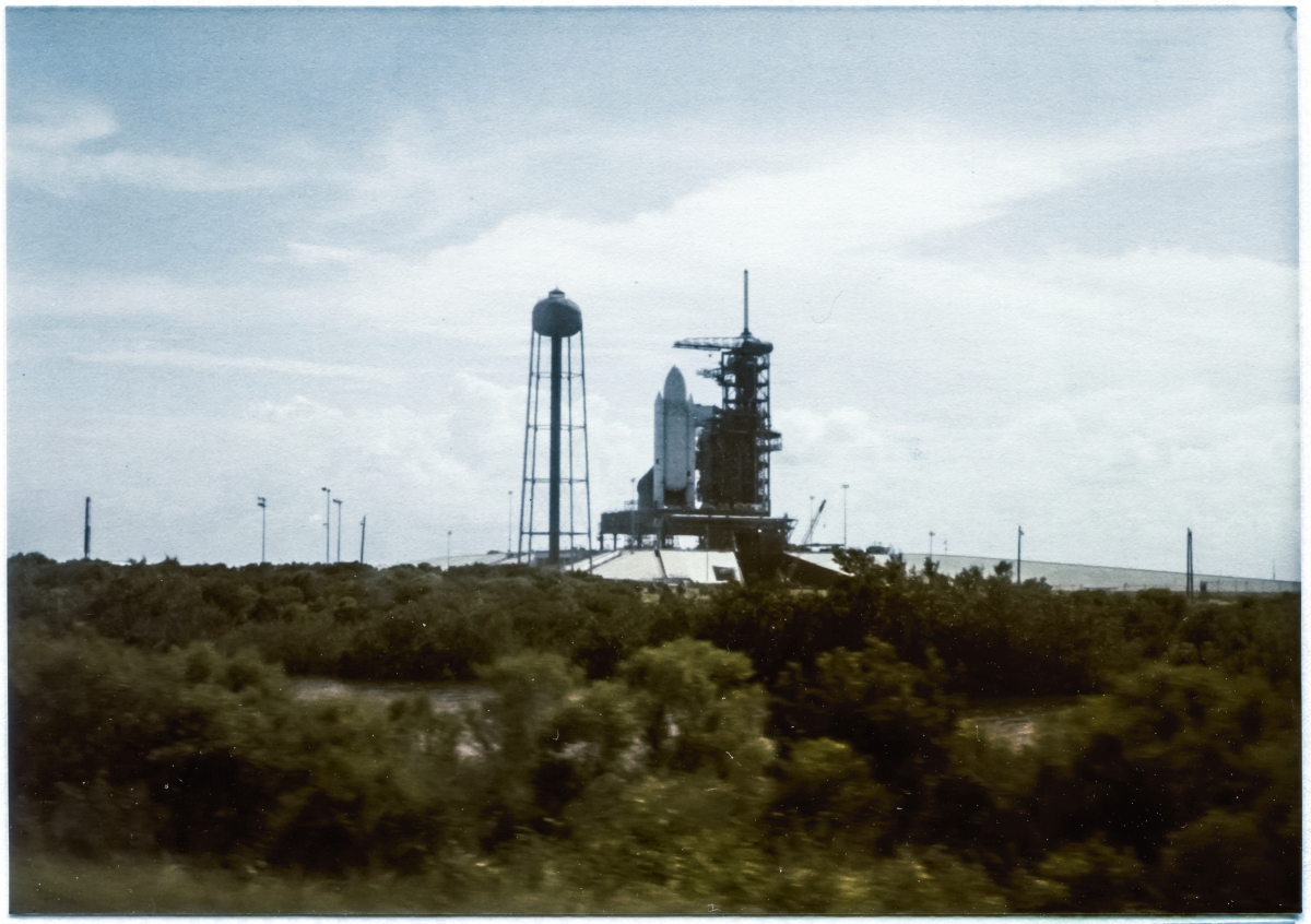 Image 020. The dawning of a new age in spaceflight manifests itself in the form of an incredible gigantic flying machine like no other that had come before it, at any time, at any place. Colombia, sitting in its launch position at the Launch Pad on top of the MLP with the RSS rolled back in its de-mate position, as seen driving along Beach Road past Space Shuttle Launch Complex 39-A, Kennedy Space Center, Florida, on the way to work at Pad 39-B which was still under construction at the time. Photograph by James MacLaren.